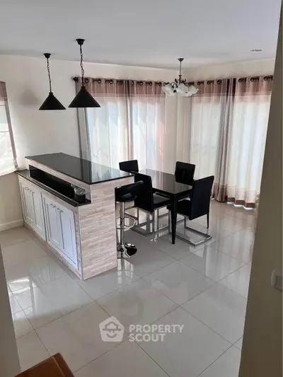 Modern kitchen with open layout and stylish dining area, featuring sleek black countertops and elegant lighting.