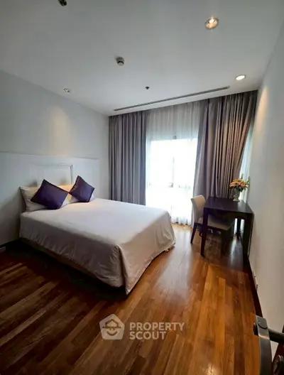 Spacious bedroom with wooden flooring and natural light in modern apartment