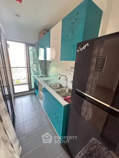 Modern kitchen with vibrant blue cabinets and balcony access, featuring a sleek black refrigerator and ample natural light.