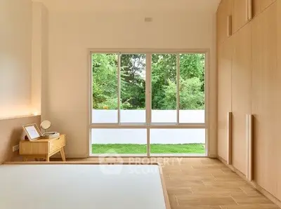 Spacious bedroom with large window and wooden flooring overlooking lush greenery.