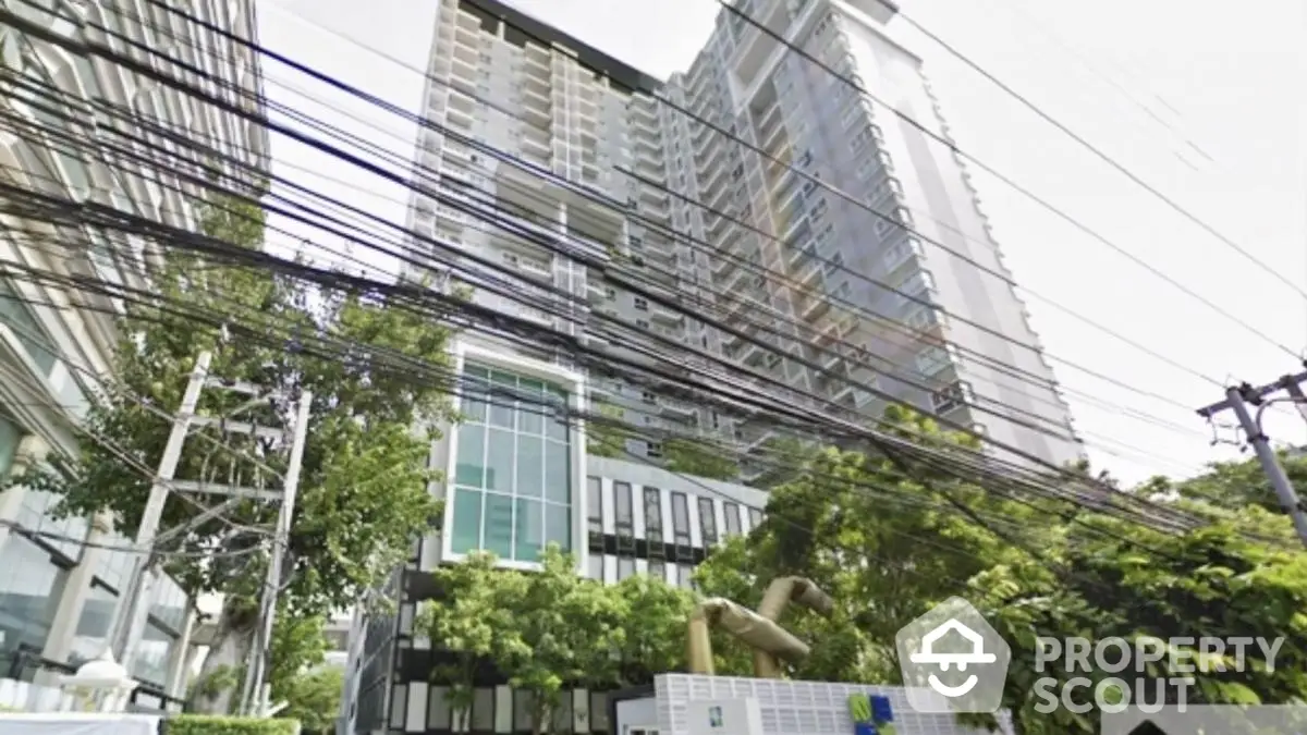 Modern high-rise condominium building with lush greenery and urban surroundings.