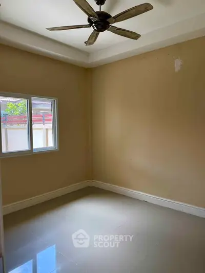 Spacious empty room with ceiling fan and large window, perfect for customization.