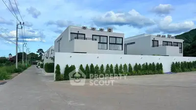 Modern minimalist white buildings with lush greenery and clear blue sky, ideal for contemporary living.