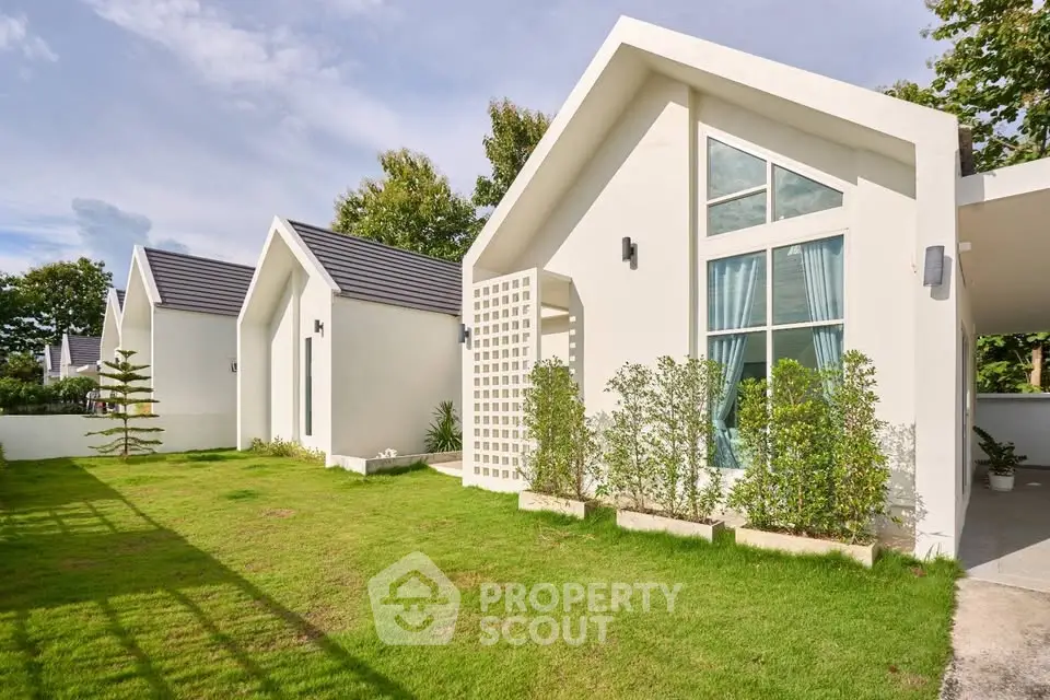 Modern white houses with lush green lawns and large windows in a serene neighborhood.