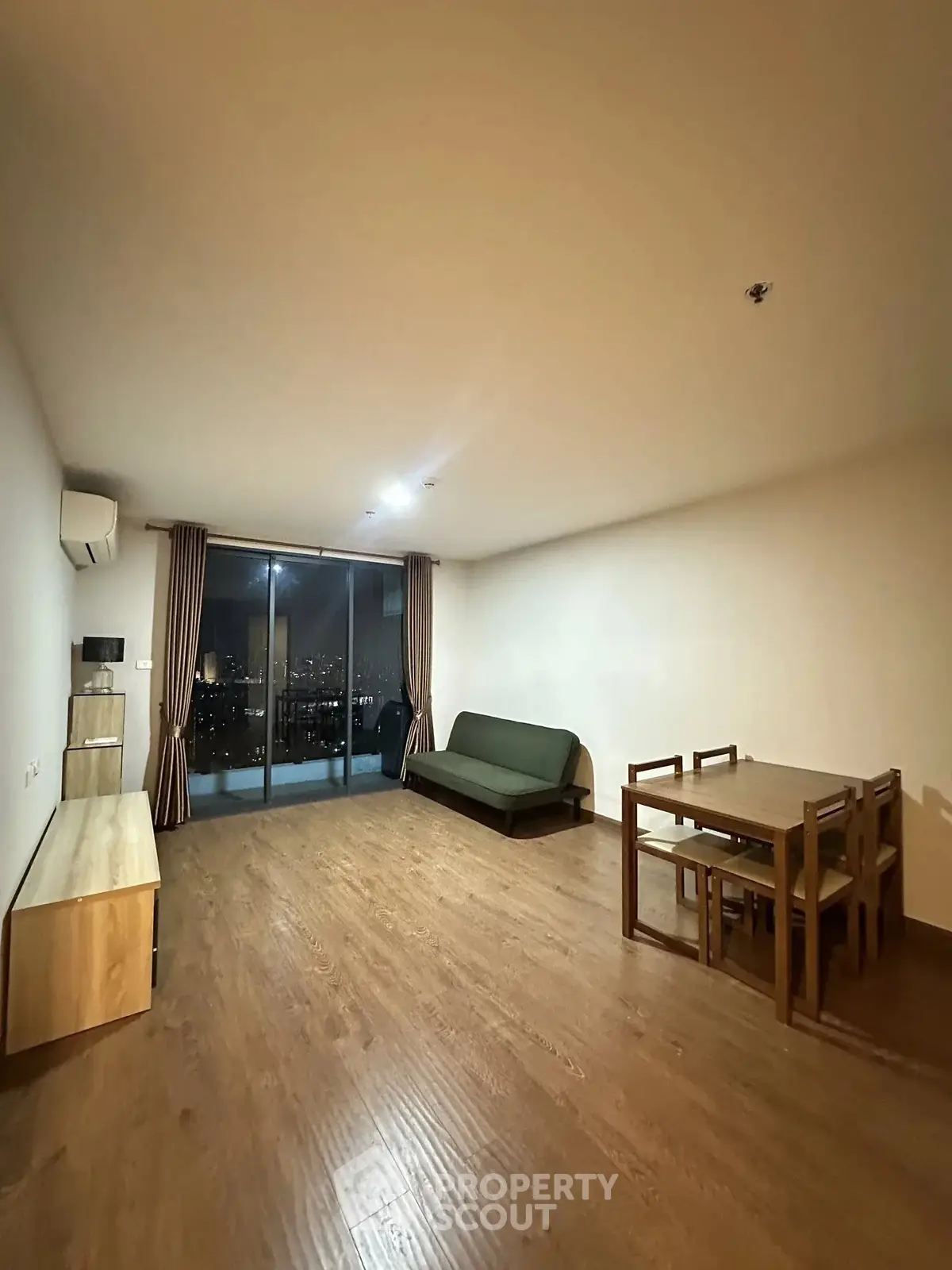 Spacious living room with wooden flooring and city view, featuring a sofa and dining table.
