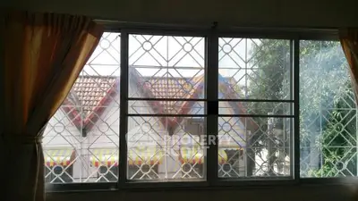 Charming window view with decorative grills overlooking tiled rooftops and lush greenery.
