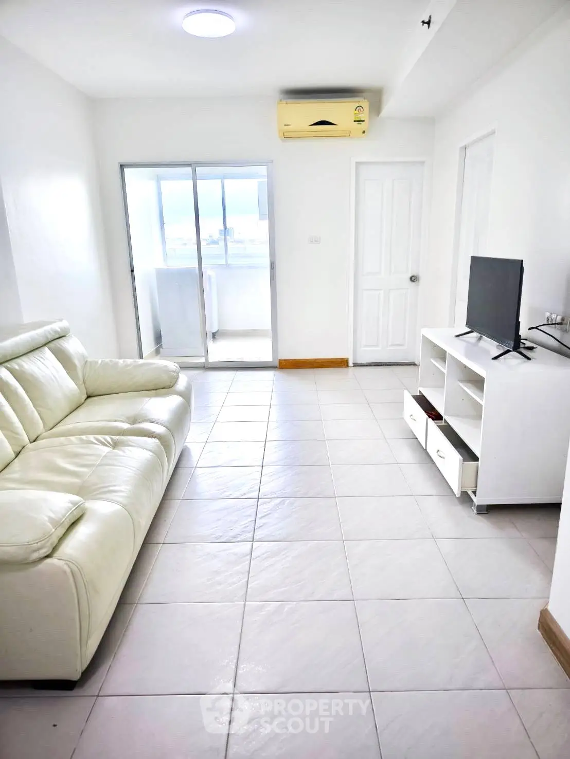 Bright living room with white leather sofa, TV stand, and sliding glass door to balcony.