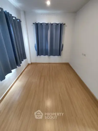 Spacious empty room with wooden flooring and blue curtains, ideal for customization.
