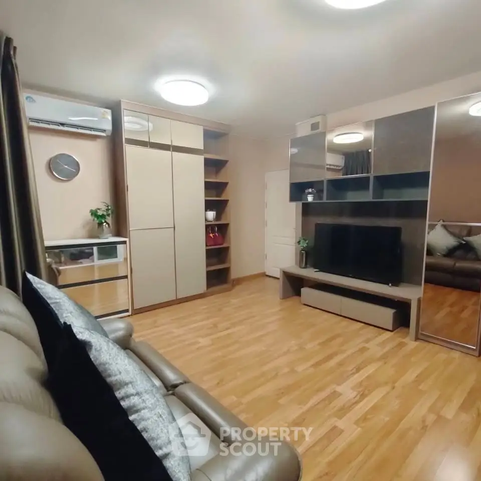 Modern living room with sleek furniture and wooden flooring, featuring a stylish entertainment center and cozy seating.