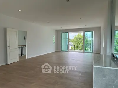 Spacious open-plan living room with large windows and balcony access, featuring modern flooring and natural light.