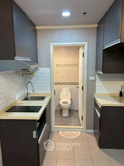 Modern kitchen with sleek cabinetry and integrated appliances leading to a compact bathroom.