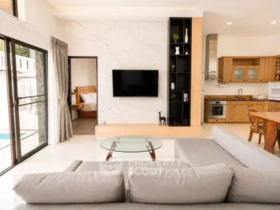 Spacious modern living room with open kitchen and pool view, featuring elegant decor and natural light.