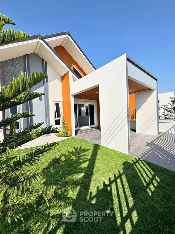 Modern architectural home exterior with vibrant orange accents and lush green lawn.