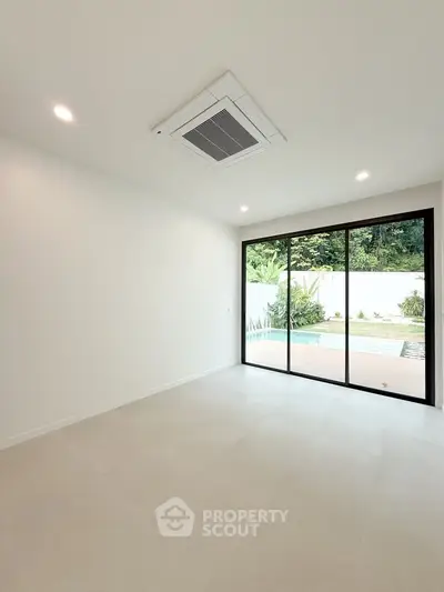 Spacious modern room with large windows overlooking a serene pool and lush greenery.