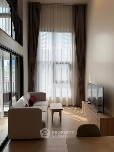 Modern living room with high ceilings and large windows, featuring a cozy sofa and flat-screen TV.