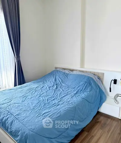 Cozy bedroom with blue bedding and natural light from large window, perfect for relaxation.