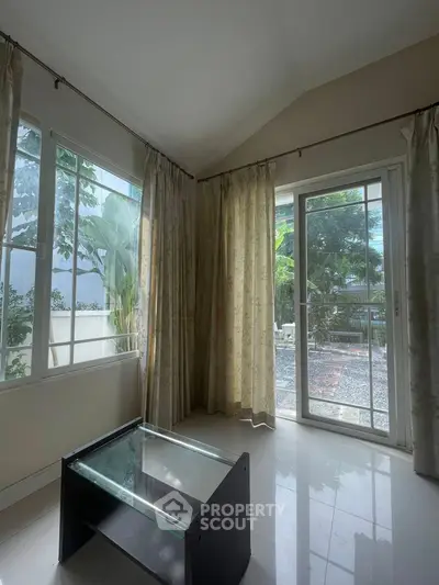 Bright living room with glass coffee table and garden view through large windows.