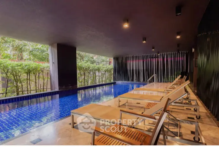 Luxurious indoor pool area with modern lounge chairs and lush greenery view.