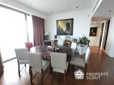 Elegant dining room with large round table and art decor, featuring natural light and wooden flooring.