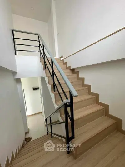 Modern staircase with sleek metal railings and wooden steps, leading to a bright, airy upper level in a contemporary home.