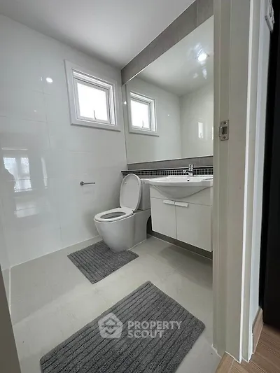 Modern bathroom with sleek design and large mirror, featuring white fixtures and natural light.
