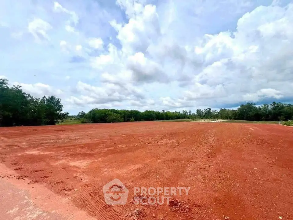 Expansive red soil land plot under a vast blue sky, ideal for development opportunities.