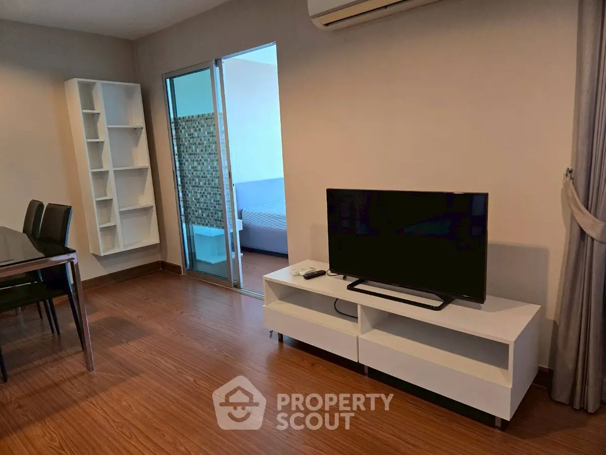 Modern living room with TV and dining area, featuring sleek furniture and wooden flooring.
