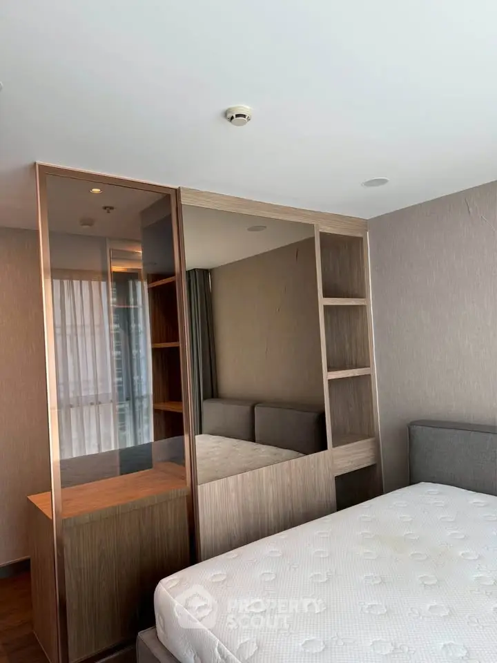Modern bedroom with built-in wooden shelving and large mirror, featuring a comfortable mattress.