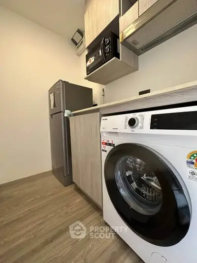 Modern kitchen with washing machine, fridge, and sleek cabinetry in compact layout.