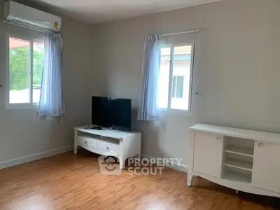 Spacious living room with wooden flooring and modern furniture, featuring a TV and air conditioning.