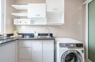 Modern kitchen with sleek cabinetry and built-in washing machine, featuring a minimalist design and ample natural light.
