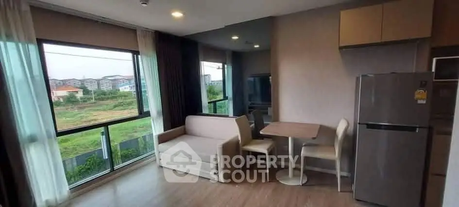 Modern living room with large windows and dining area, featuring a cozy sofa and sleek refrigerator.