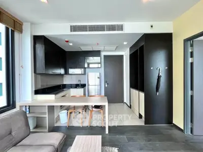 Modern living room with sleek kitchen and dining area, featuring stylish black cabinetry and natural light.
