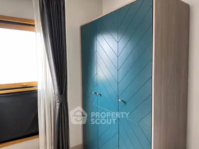 Stylish modern bedroom with elegant blue wardrobe and large window for natural light.