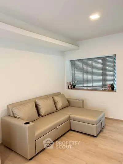 Modern living room with beige sectional sofa and large window with blinds.