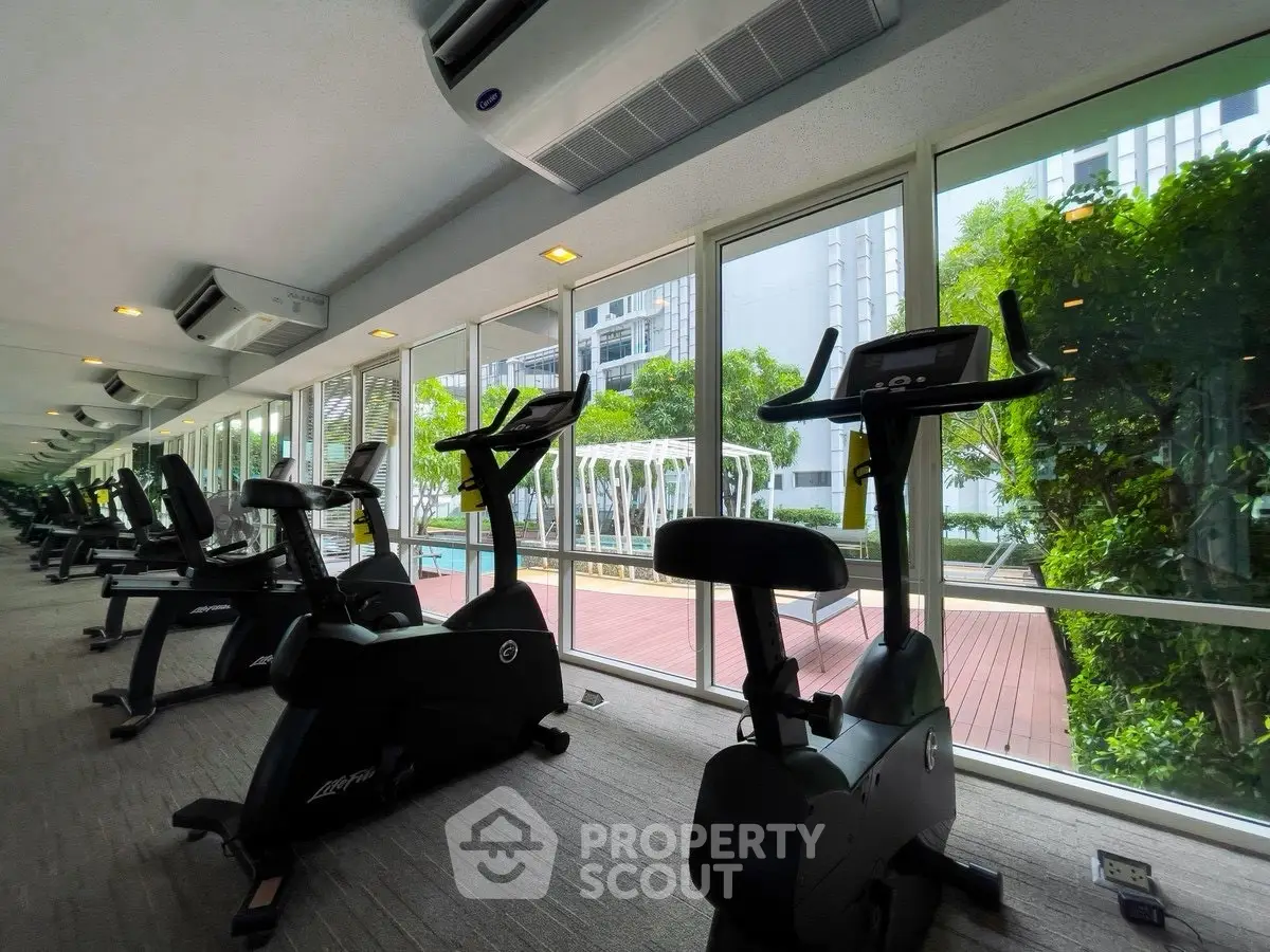 Modern gym with exercise bikes and large windows overlooking greenery.
