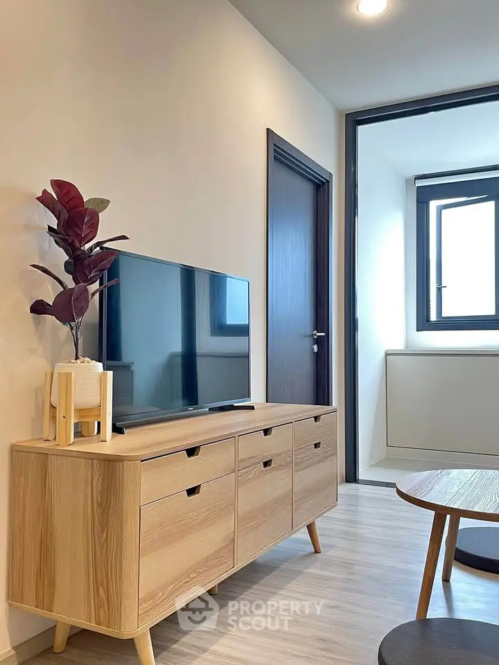 Modern living room with sleek wooden furniture and large TV, featuring minimalist decor and natural light.