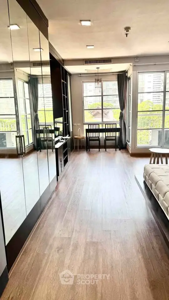 Spacious modern living room with large windows and mirrored wall, offering abundant natural light and city views.