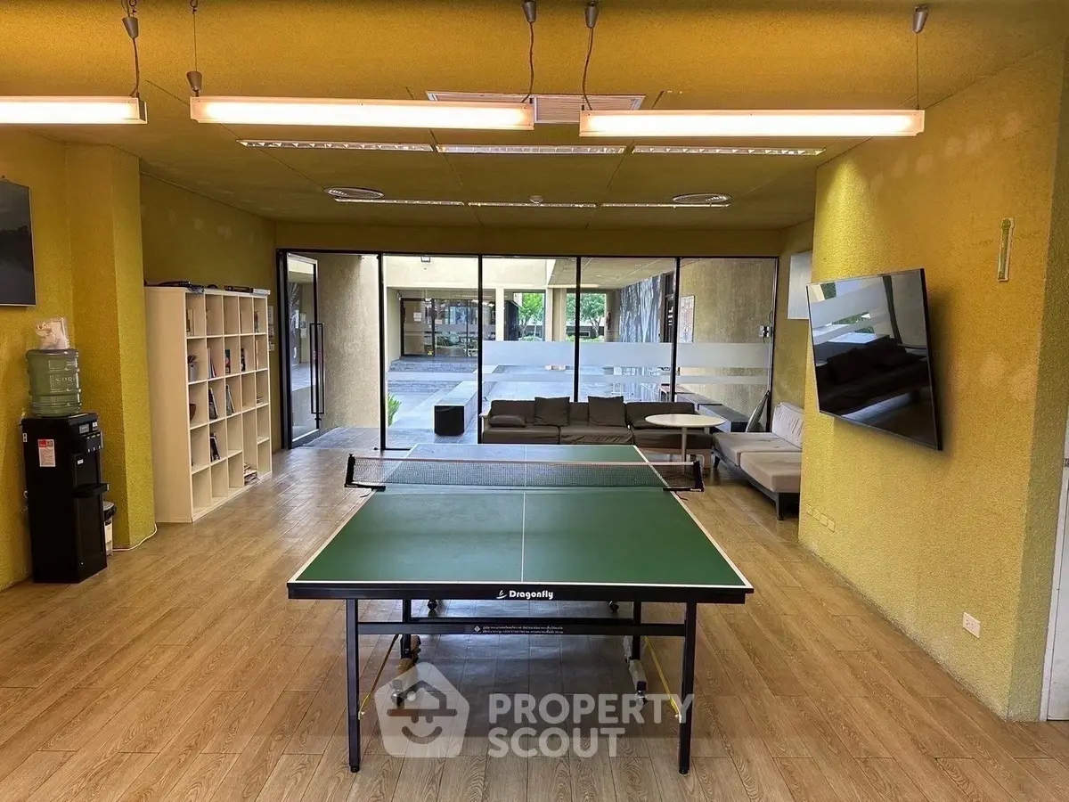 Spacious common area with table tennis, lounge seating, and large TV in modern building.