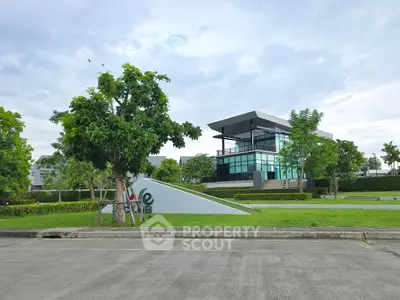Modern building with lush green surroundings and spacious parking area.