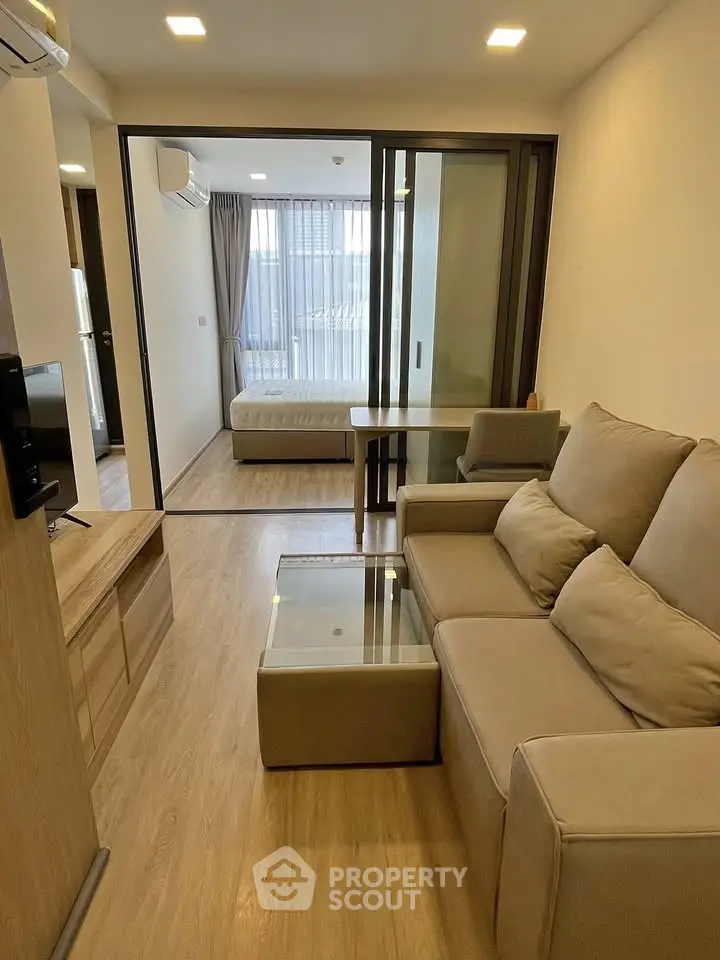 Modern apartment interior with cozy living room and bedroom separated by glass doors.