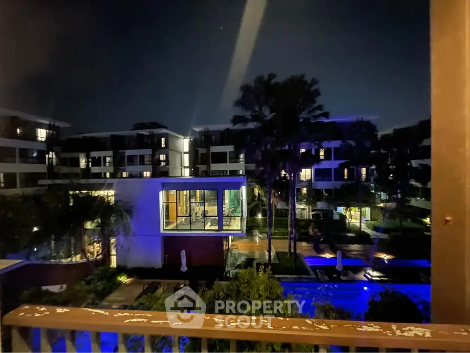 Stunning night view of modern apartment complex with illuminated pool and lush greenery.