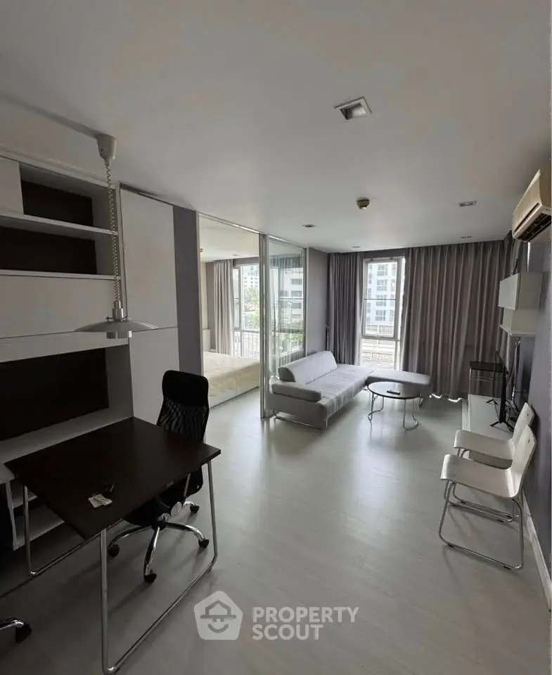 Modern open-plan living room with study area and large windows in urban apartment.