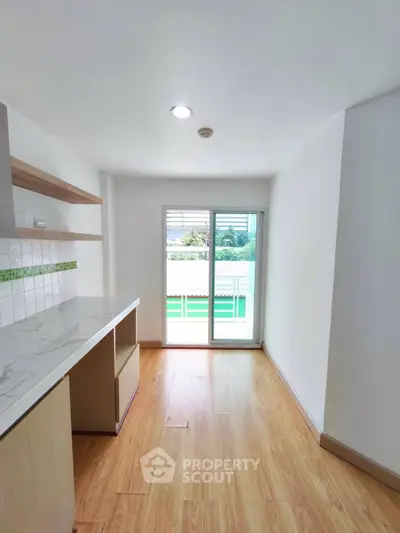 Bright kitchen with wooden flooring and sliding glass doors leading to balcony.