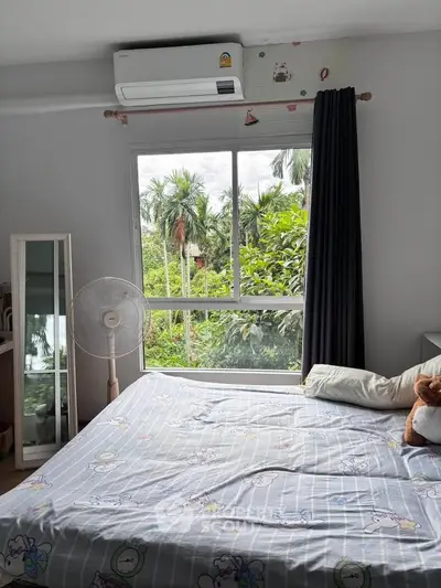 Cozy bedroom with large window offering lush green view and air conditioning.