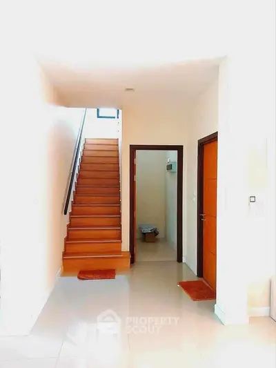 Bright modern hallway with wooden staircase and sleek white tiles