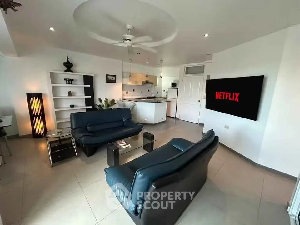 Modern living room with sleek furniture and open kitchen layout, featuring a large TV and stylish decor.