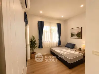 Cozy bedroom with single bed, wooden flooring, and natural light from window.