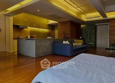 Modern open-plan living room with stylish kitchen and cozy seating area, featuring warm lighting and wooden flooring.