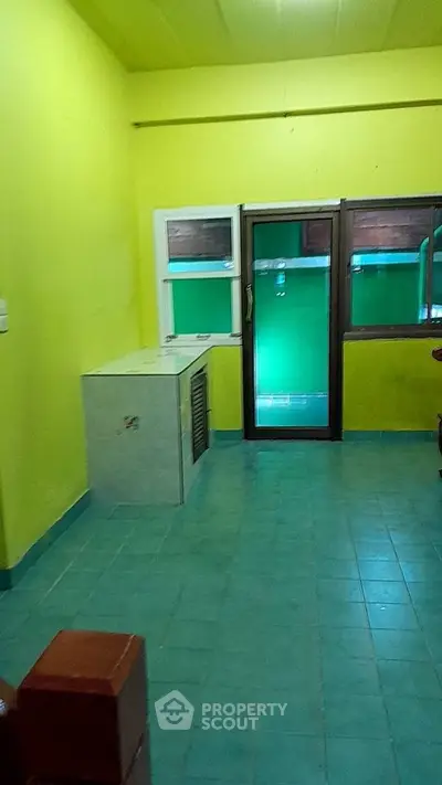 Vibrant room with green tiles and yellow walls, featuring a large window and door for natural light.